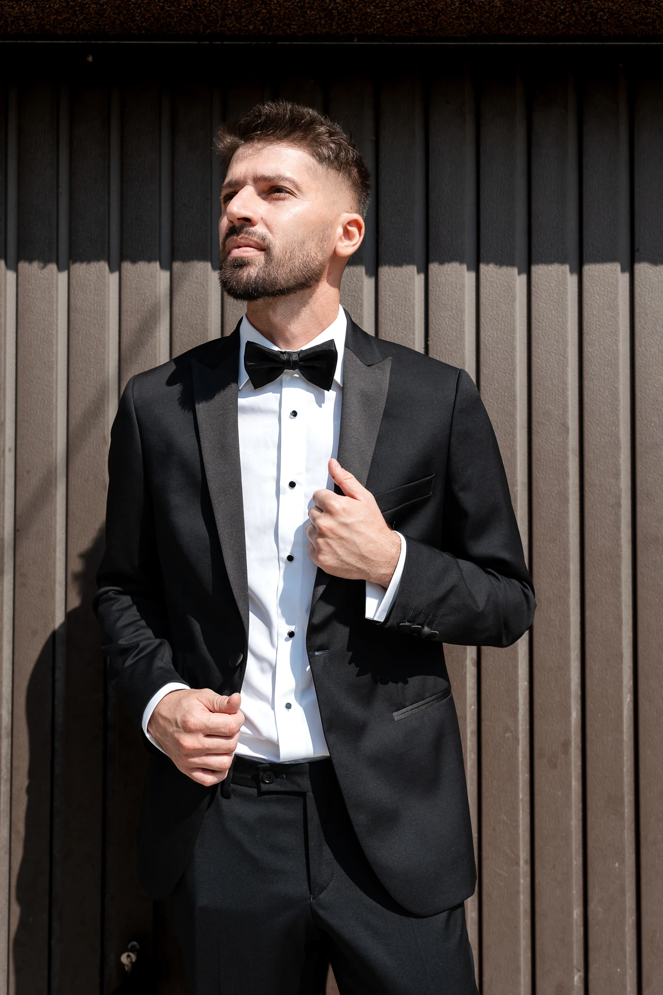 Portret de mire în Hârșova: Ionuț în costum negru și papion, în fața unei uși din lemn